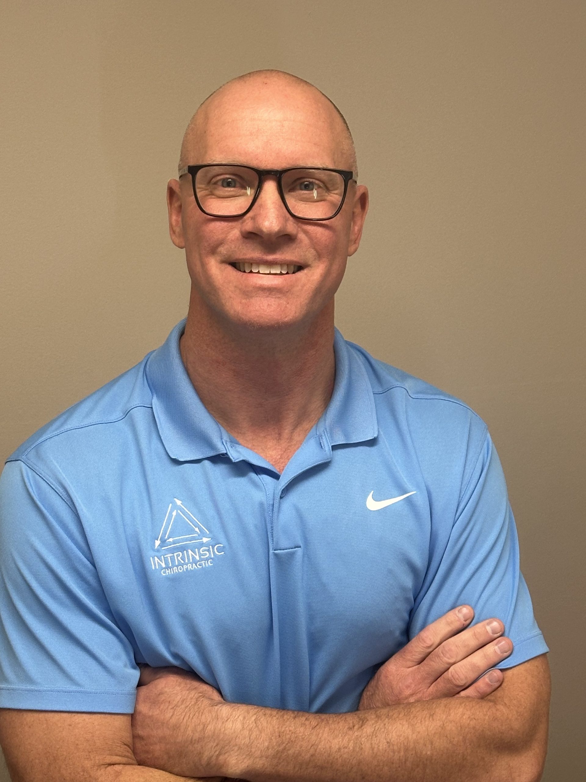 Glasses smiling Clinic owner and chiropractor standing with arms crossed, wearing a branded chiropractic polo